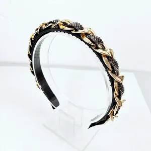 Close-up of baroque headband with gold chains and dark gray rhinestones on black fabric