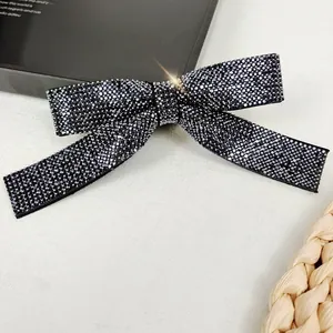 Detailed close-up of a sparkling bow hair clip with dark grey rhinestones on a textured base