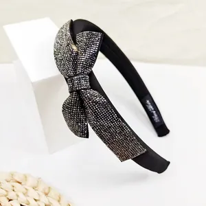 Detailed view of black satin headband with sparkling rhinestone bow and interior branding