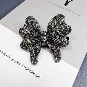 Elegant black rhinestone bow hair clip with silver beaded edges on magazine background