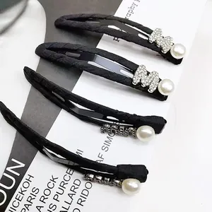 Détail de barrettes en tissu noir avec logo M en strass et perles élégantes