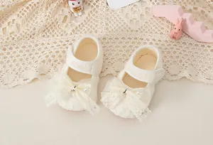 Dettaglio di scarpe per neonata in pizzo con fiocco e decorazioni di perle fini