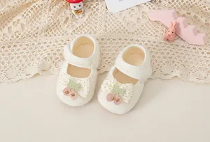 Dettaglio scarpe neonata in peluche color crema con fiocco e decorazione a ciliegia