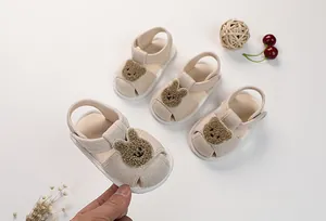 Detail of infant beige cotton sandals featuring plush bear and rabbit toe decorations