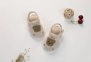 Close-up of beige cotton baby sandals with cute bear patch and secure toe protection
