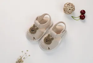 Close-up of baby beige cotton sandals with cute plush rabbit patch and velcro strap