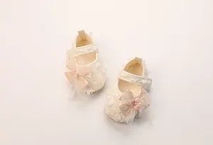 Detail eines Baby-Spitzenschuhs mit 3D-Blütenblättern, Pailletten und rosa Netzschleife
