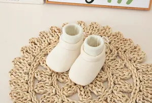 Close-up of off-white knitted baby walk shoes on a woven mat with ribbed cuff details