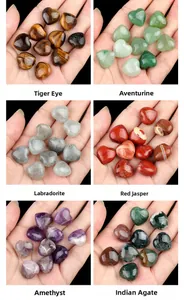 Hand holding six natural crystal heart stones including Amethyst and Tiger Eye for scale