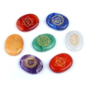 Set of 7 chakra natural crystal oval stones with gold engraved symbols on white background
