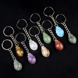 Nine crystal beetle keychains carved from tiger eye and amethyst on black background