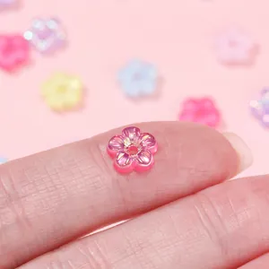 Macro shot of tiny pink 5-petal acrylic flower beads with rainbow UV coating for DIY crafts