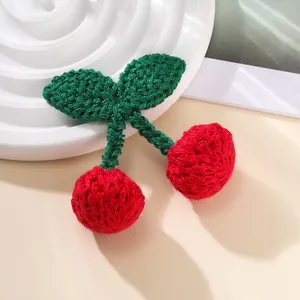Detail of handmade crochet cherry charm featuring red yarn fruit and green leaves