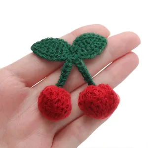 Handheld detail of mini handmade crochet cherry ornament with green leaves and red yarn