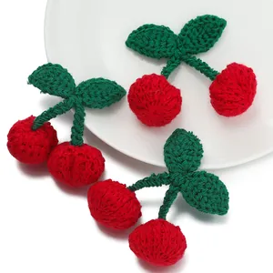 Close-up of handmade knitted cherry pendants with vibrant red yarn and green leaves