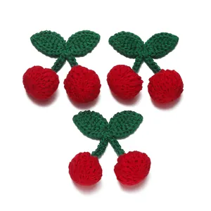 Detail of three pairs of handcrafted crochet cherries with red fruits and green leaves