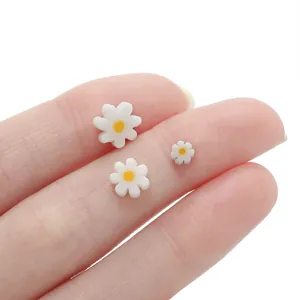 Macro view of white daisy glass beads in three sizes placed on a fingertip for DIY