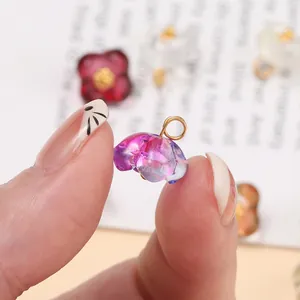 Macro view of a small gradient glass flower charm with a gold ring held by fingers
