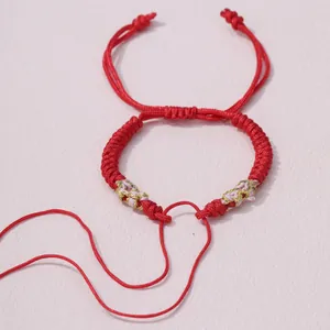 Makrodetail eines handgeflochtenen roten Armbands mit rosa und goldenen Metallfäden