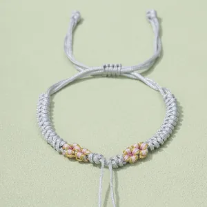 Detail von handgewebtem Armband mit rosa Blumenakzenten und verstellbarem Gleitknoten