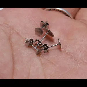 Golden stainless steel flat head earring studs with butterfly backs on a hand