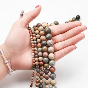 Hand mit verschiedenen Größen natürlicher Picasso-Jaspis-Steinperlen für DIY-Schmuck