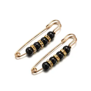 Vista de detalle de dos broches imperdibles dorados con perlas negras y piedras brillantes
