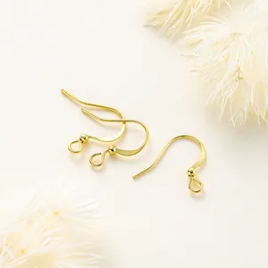 Detalle de tres ganchos para pendientes chapados en oro sobre un fondo blanco minimalista