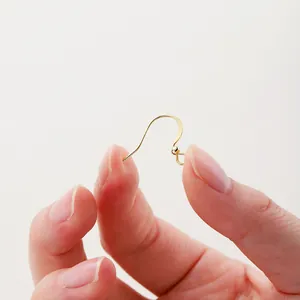 Vista macro de ganchos para pendientes dorados para hacer joyas DIY entre los dedos