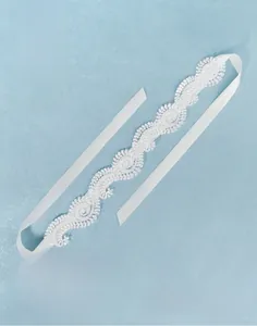 Close-up of a white lace bridal headband featuring intricate scroll patterns and satin ribbons