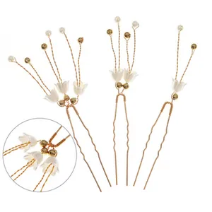 Detail view of three gold U-shaped hair pins with white lily of the valley and pearls