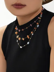 Detail einer mehrlagigen Goldkette mit bunten unregelmäßigen Natursteinperlen auf schwarzem Pulli