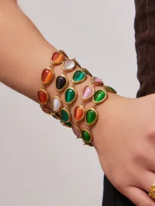 Detailansicht goldener Armbänder mit bunten Tropfen-Katzenaugensteinen am Handgelenk