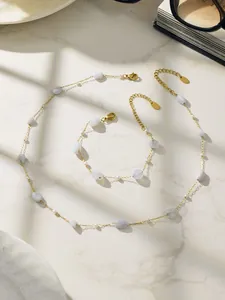 Detailaufnahme von vergoldeter Perlenkette und Armband mit hellblauen Steinen auf Marmor