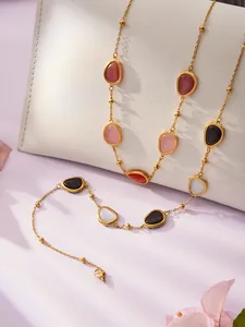 Detail von bunten facettierten Steinen an langer Goldkette, über weißer Ledertasche drapiert