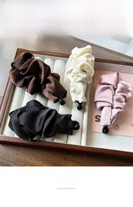 Detail showing elegant satin pleated banana hair clips in four soft colors on a jewelry tray