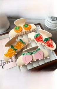 Detail view of acetate fruit hair claws featuring strawberry and peach designs on a tray