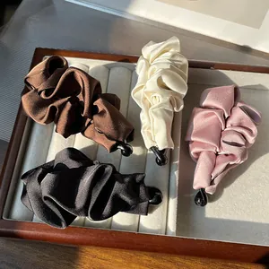 Elegant satin pleated banana hair clips in brown, white, black and pink on a wooden tray