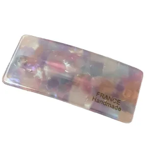 Minimalist rectangular hair clip with pastel marble texture and gold lettering on white