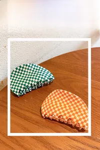 Nahaufnahme von halbrunden Schachbrett-Haarklammern in Grün und Orange auf Holztisch
