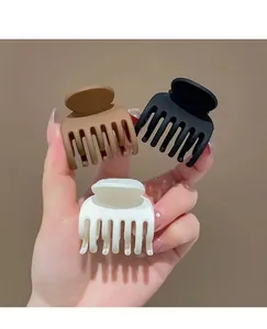 Tre fermagli per capelli opachi nei colori marrone, nero e crema tenuti in mano
