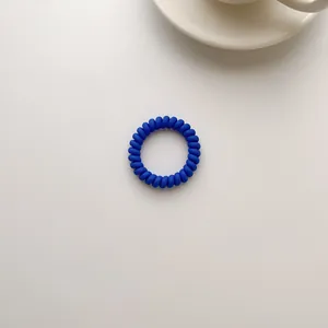 Close-up of a deep blue spiral hair tie in a minimalist phone cord design on white