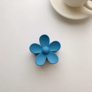 Close-up of a blue matte five-petal flower hair claw clip on a minimalist white desk