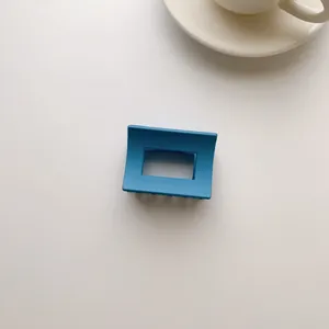 Detail view of square hollow hair claw clip in matte blue finish on minimalist surface