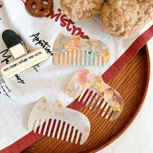 Three cute cat-shaped acetate hair combs with marble patterns on a wooden tray