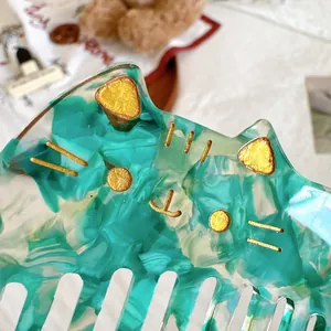 Detail view of cat-shaped acetate hair comb with blue-green marble texture and gold accents