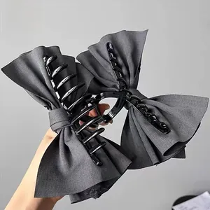 Close-up of dark grey fabric bow hair claw clip with black plastic teeth detail