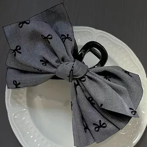 Detail view of a large grey fabric bow hair claw clip with black butterfly print patterns