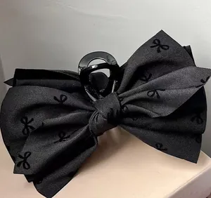 Macro detail of large black fabric bow hair claw clip showing textured ribbon material