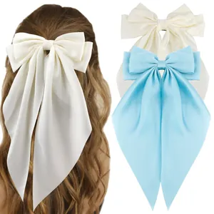 Detail view of large satin bow hair clips in beige and light blue with long streamers